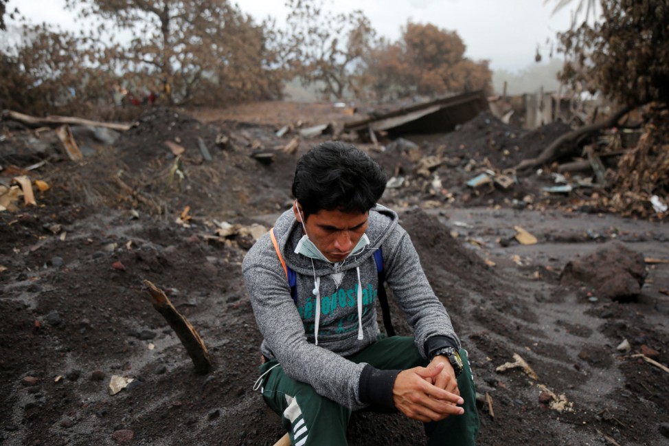 A resident sits on the rubble as people continue to search for remains of victims after the eruption of the Fuego volcano in Escuintla, Guatemala