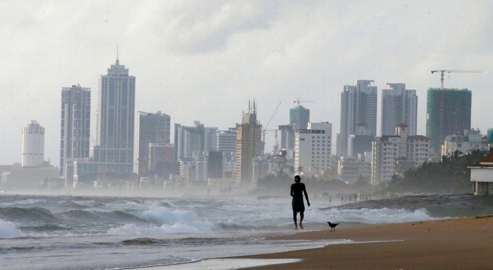 A man walks along a beach, against the backdrop of Colombia's Financial City, Sri Lanka