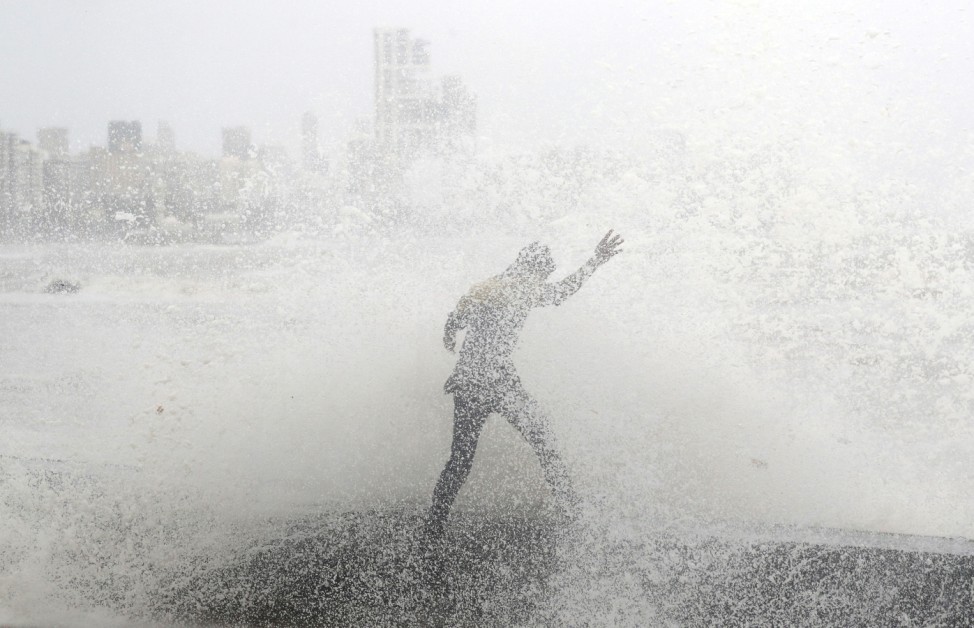 A man loses his balance as he gets drenched by a large wave during high tide at a seafront in Mumbai