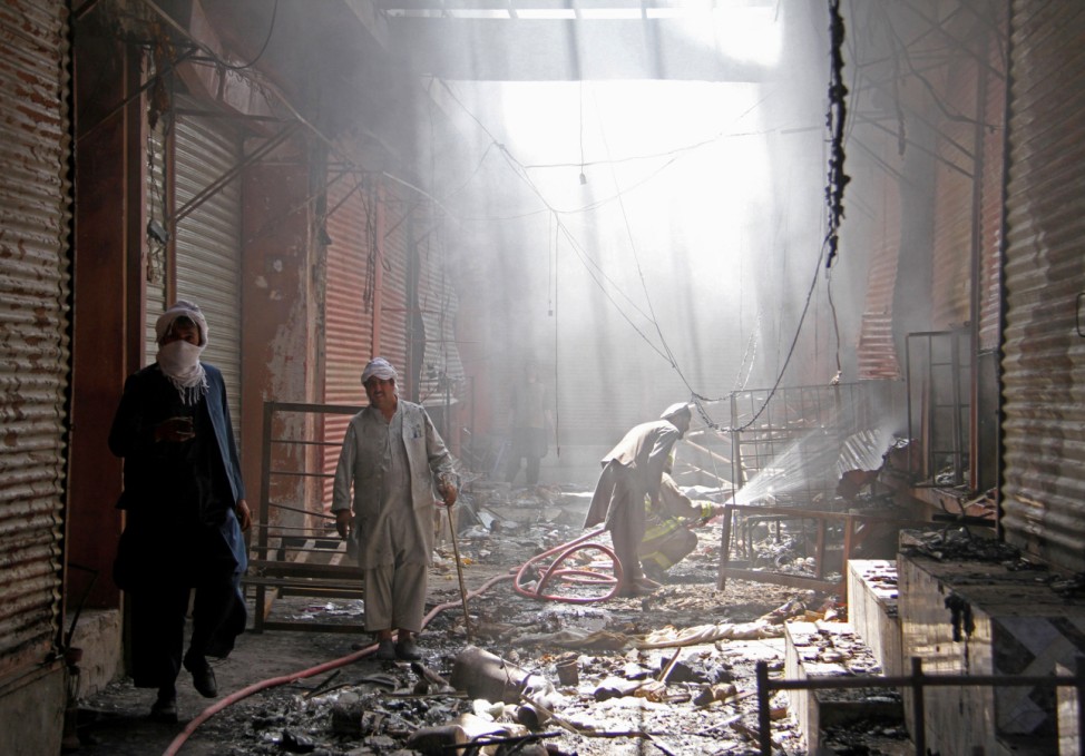 An Afghan firefighter sprays water on burning shops after a Taliban attack in Ghazni city,