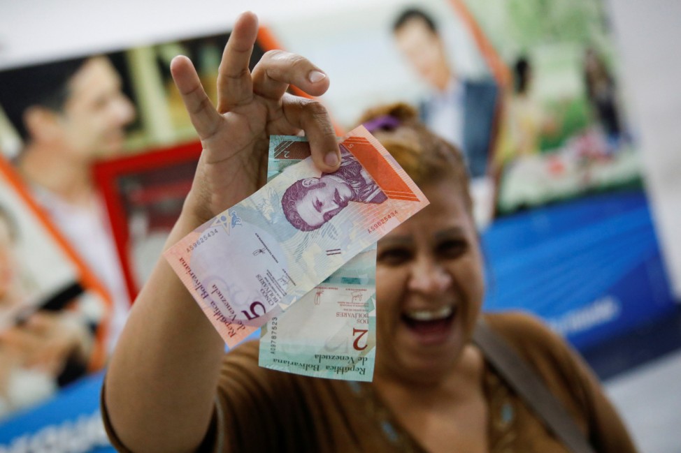 A woman smiles while she shows the new two and five Bolivar Soberano (Sovereign Bolivar) bills, after she withdrew them from an automated teller machine (ATM) at a Mercantil bank branch in Caracas