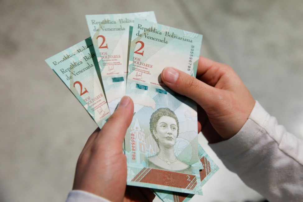 A woman shows the new two Bolivar Soberano (Sovereign Bolivar) bills, after she withdrew them from an automated teller machine (ATM) at the Banesco bank headquarters in Caracas