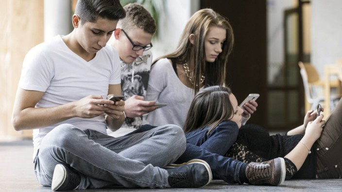 Vier Jugendliche sitzen auf dem Boden und schauen in ihr Smartphone model released Copyright xMEV
