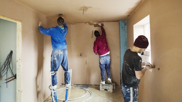 Three men two plasterers wearing stilts smoothing fresh plaster high up on the walls of a house und