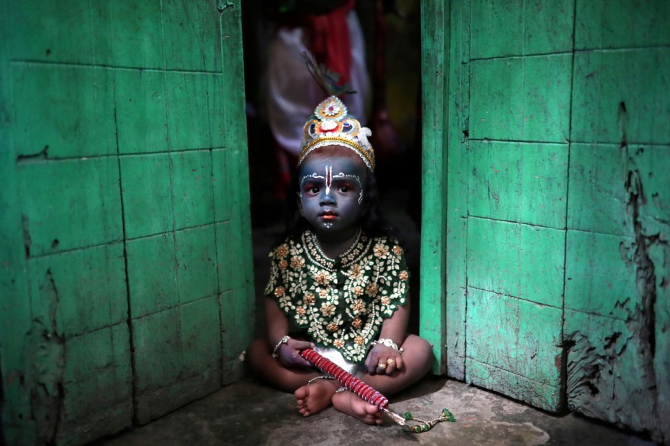A child sits on a doorstep, dressed as Lord Krishna during Janmashtami festival, which marks the birth anniversary of Lord Krishna in Dhaka