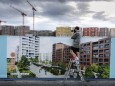 Ein Mann steht auf einer Leiter vor einer Informationswand zum Wohnungsbau und fotografiert eine Bau