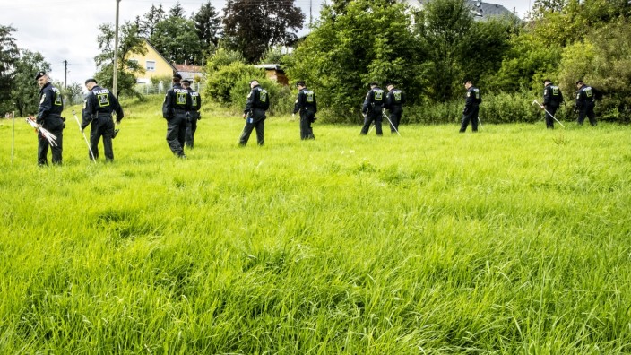 Raubmord von Meiling: Polizisten durchkämmen die Wiese vor dem Anwesen im Seefelder Ortsteil Meiling, um Spuren der Täter zu sichern.