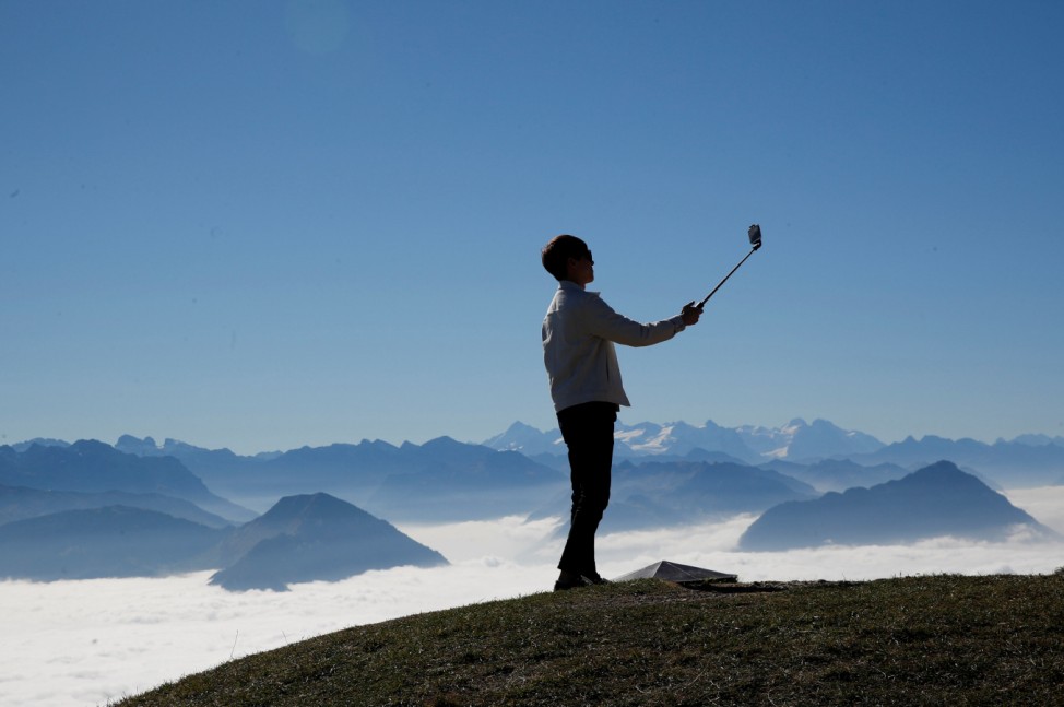 A man takes a picture with his smartphone mounted on a selfie stick during sunny autumn weather near the peak of Mount Rigi