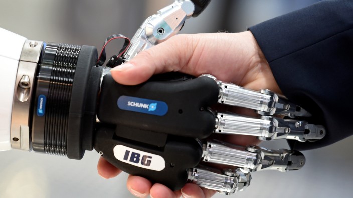 A visitor shakes hands with a humanoid robot at the booth of IBG at Hannover Messe, the trade fair in Hanover