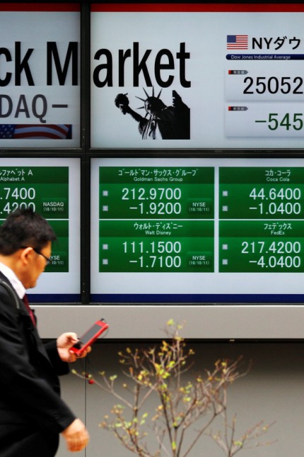 A man walks past electronic boards showing Dow Jones Industrial Average and and NASDAQ average in Tokyo