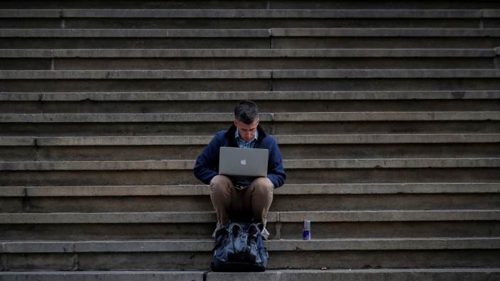 A man uses his Apple laptop on the steps of Federal Hall on Wall St. in the financial district of New York