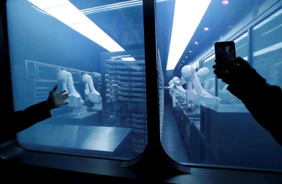 A customer takes a picture as robotic arms collect pre-packaged dishes from a cold storage, done according to the diners' orders, at Haidilao's new artificial intelligence hotpot restaurant in Beijing