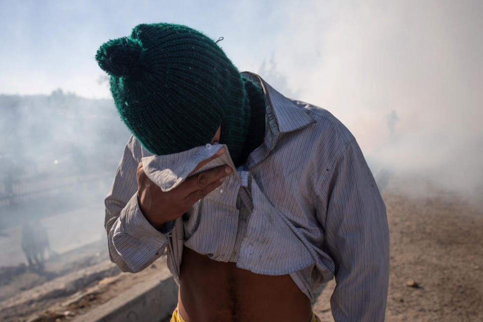 A migrant, part of caravan from Central America, covers face from tear gas released at the U.S. border with Mexico in Tijuana