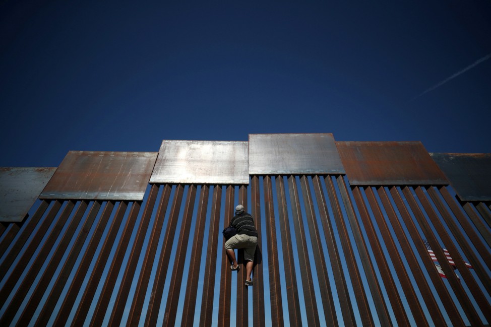 A migrant climbs the fence between Mexico and the United States in Tijuana