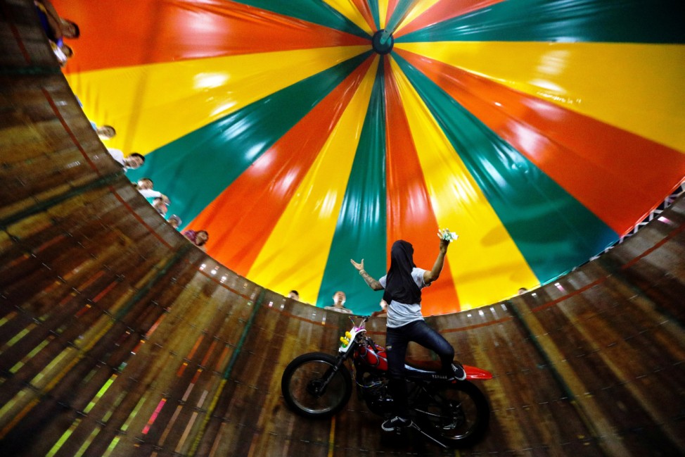 A stuntman covering his face rides a motorcycle inside the 'Well of Death' attraction during a fair in Bangkok