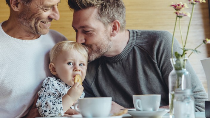 Gay couple cuddling with their baby in cafe model released Symbolfoto property released PUBLICATIONx