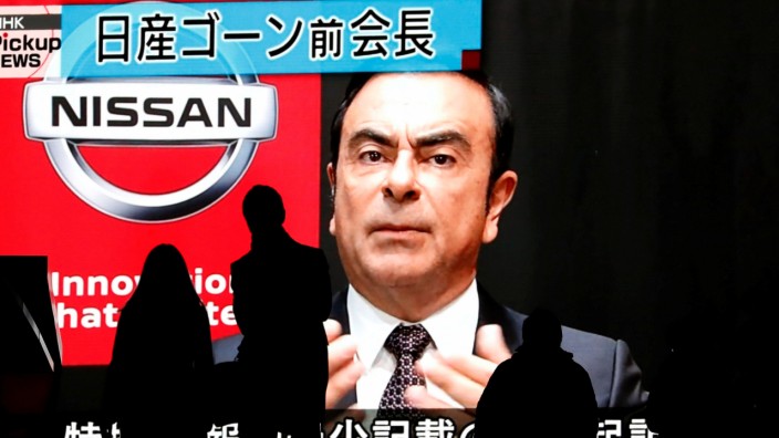 Passersby are silhouetted as a huge street monitor broadcasts news reporting ousted Nissan Motor chairman Carlos Ghosn's indictment and re-arrest in Tokyo