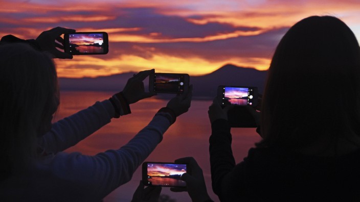 Menschen fotografieren den Sonnenuntergang mit ihrem Smartphone bei Luino Lago Maggiore Lombardei