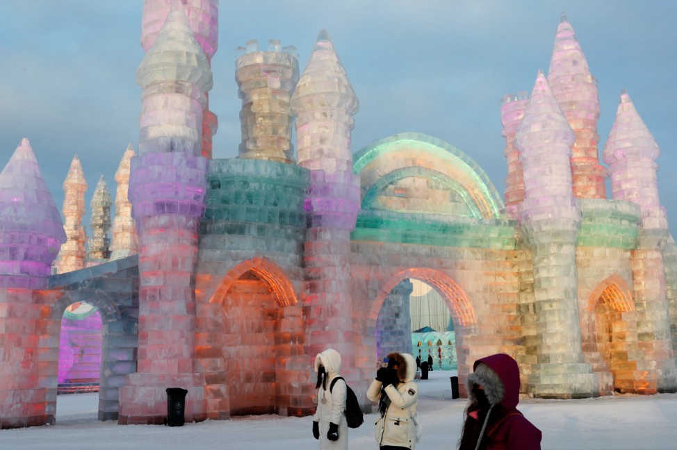 Visitors stand in front of ice sculptures illuminated by colored lights at annual ice festival, in the northern city of Harbin, Heilongjiang province