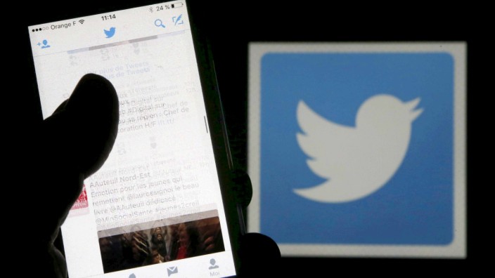 FILE PHOTO: A man reads tweets on his phone in front of a displayed Twitter logo in Bordeaux, southwestern France