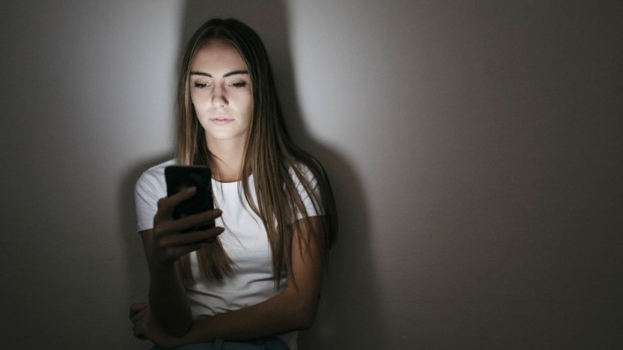 Young woman at home sitting on floor using cell phone in the dark model released Symbolfoto property
