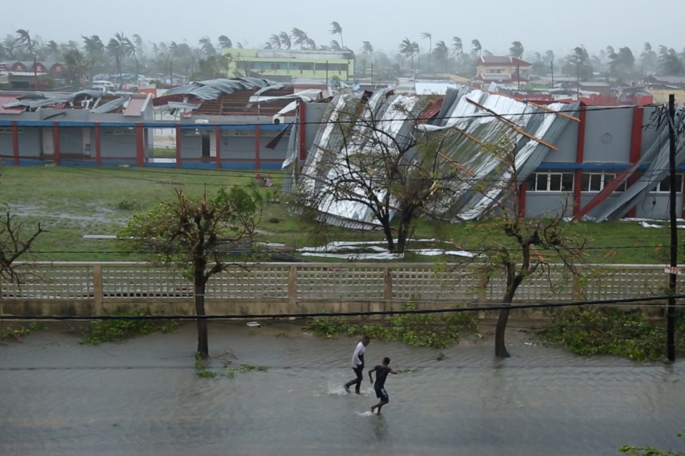 People walk down a flooded road next to buildings damaged by Cyclone Idai in Beira