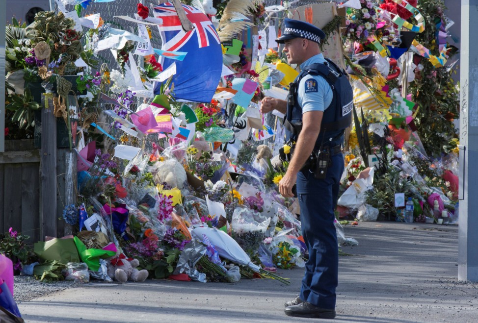 A police officer stands near flowers and objects place near the police cordon for the Linwood Islamic Centre, as people gather to support a remembrance for the victims of last week's mosque shooting in Christchurch
