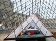 Airbnb employees pose on a bed under the glass Pyramid during a rehearsal at the Louvre museum in Paris