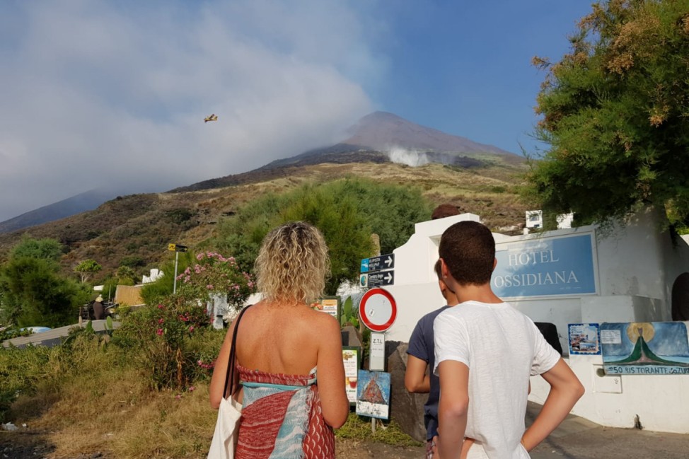Tourists watch as smoke rises from Stromboli volcano after an eruption started forest fires, in Stromboli