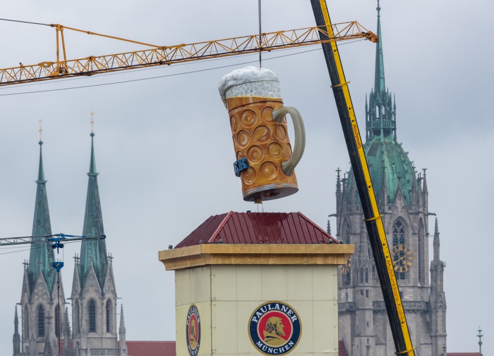Ein übergroßer Bierkrug wird mit einem Kran auf der Theresienwiese beim Aufbau des Oktoberfestes 2019 in München an seinen Platz gehoben.