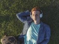 Redheaded young man with headphones lying on grass model released Symbolfoto PUBLICATIONxINxGERxSUIx