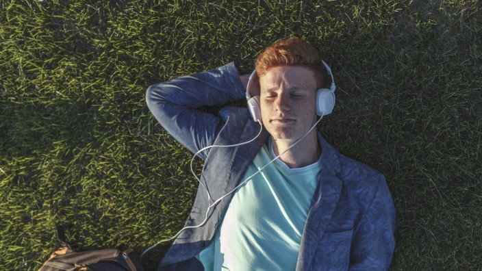 Redheaded young man with headphones lying on grass model released Symbolfoto PUBLICATIONxINxGERxSUIx