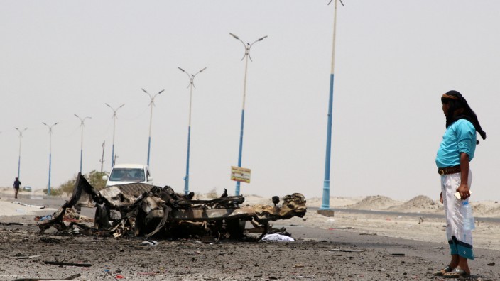 A man stands past the wreckage of government forces vehicles destroyed by UAE air strikes near Aden