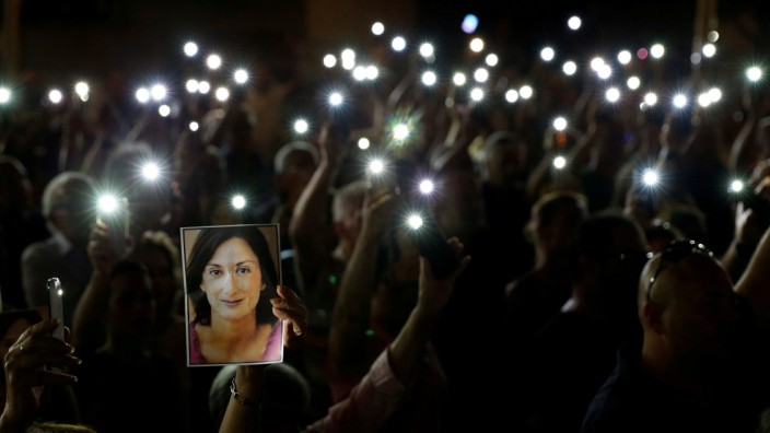 People hold up photos of assassinated anti-corruption journalist Daphne Caruana Galizia and torches on mobile phones during a vigil to mark eleven months since her murder in a car bomb, in Valletta