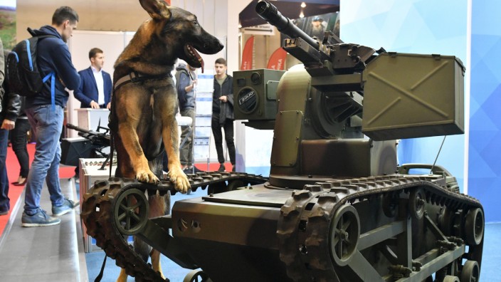 Schweiz: Seltsame Kameraden: Auf einer Waffen- und Sicherheitsmesse in Kiew steht ein Polizeihund neben einem Roboterfahrzeug mit einer Maschinenkanone.