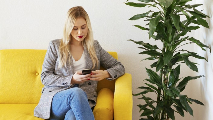 Businesswoman sitting on yellow couch using smartphone model released Symbolfoto property released