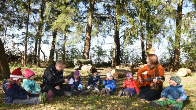 Garchinger Kindergarten: Morgenkreis im Gras: Leiterin Isabel Nefzger und Linus Brösamle, der ein freiwilliges soziales Jahr im Naturkindergarten leistet, singen und spielen mit den Kindern.