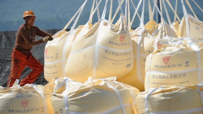Worker helps a crane transporting sacks of soda ash for export at a port in Lianyungang, Jiangsu