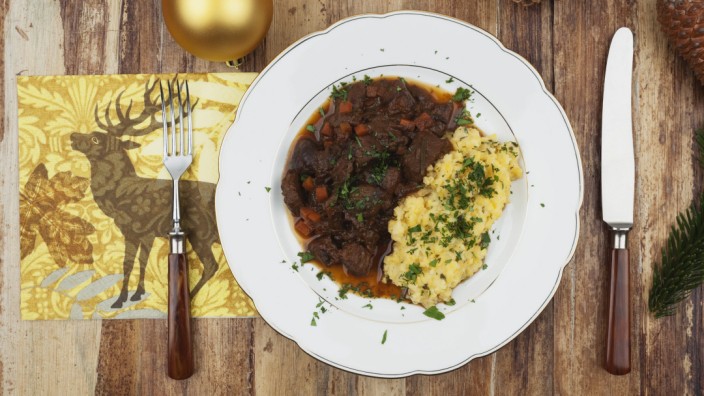 Plate of cooked venison goulash with mashed potatoes and Christmas decoration on wooden background P