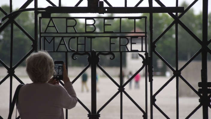 Zeitgeschichte: An der KZ-Gedenkstätte Dachau macht eine Frau mit ihrem Handy ein Foto von dem Tor mit der zynischen Aufschrift "Arbeit macht frei".