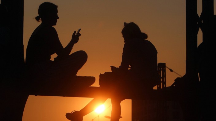 Sommerabend in München junge Frauen sitzen auf dem Geländer der Hackerbrücke und genießen den Sonne