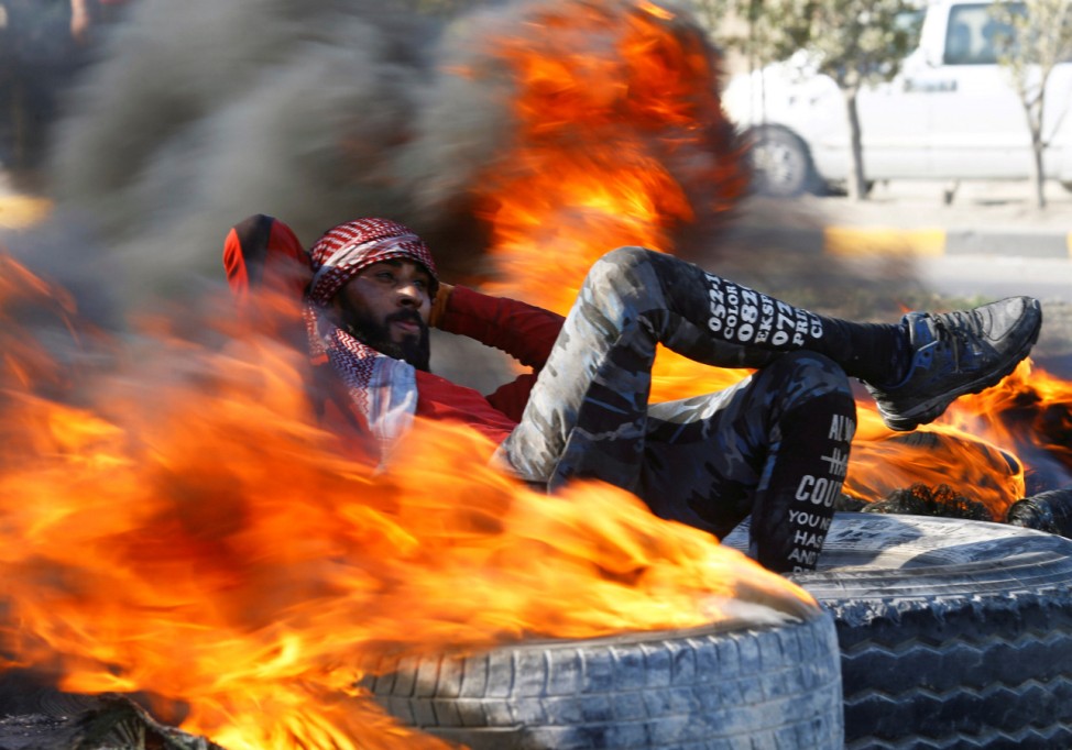 An Iraqi demonstrator sits amid burning tires blocking a road during ongoing anti-government protests in Najaf