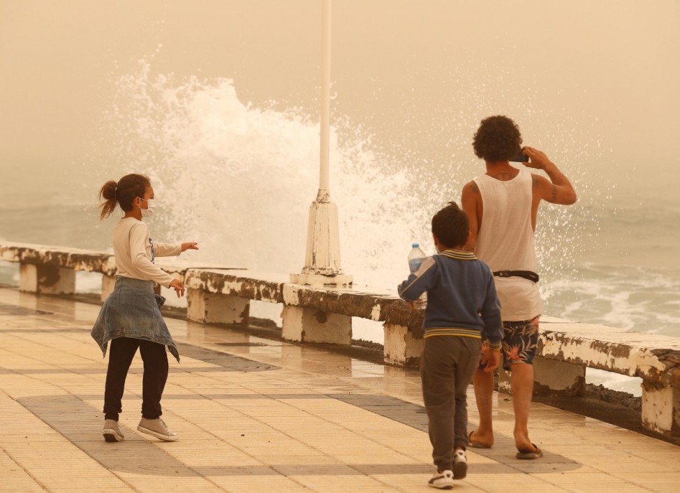 A family watches the waves during a sandstorm locally known as 'calima' in the Canary Islands, Gran Canaria
