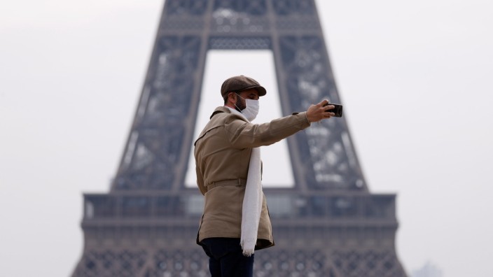 A man wearing a protective face mask makes a selfie in front of the Eiffel tower in Paris