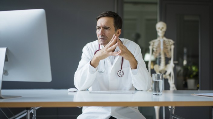 Serious doctor sitting at desk in medical practice with skeleton in background model released Symbolfoto property relea