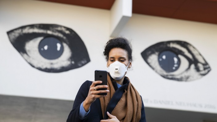 Corona-Krise: Frau mit Mundschutz schaut auf ihr Handy