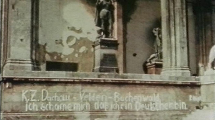 Schauplatz: Weißer Schriftzug: "KZ Dachau - Velden - Buchenwald. Ich schäme mich, daß ich ein Deutscher bin."