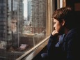 Tween boy looking out a window at tall buildings of the city outside. Toronto, ON, Canada ,model released, Symbolfoto PU