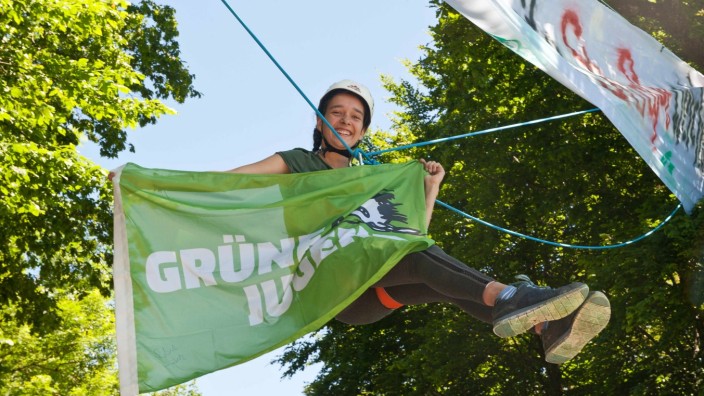 Grafing: Protest aus der Luft: Marina Ruoff hängt in einem Gurtgestell an einem Seil, das quer über die Straße zwischen die beiden Bäume geknüpft ist, die wegen der Straßenerneuerung gefällt werden sollen.