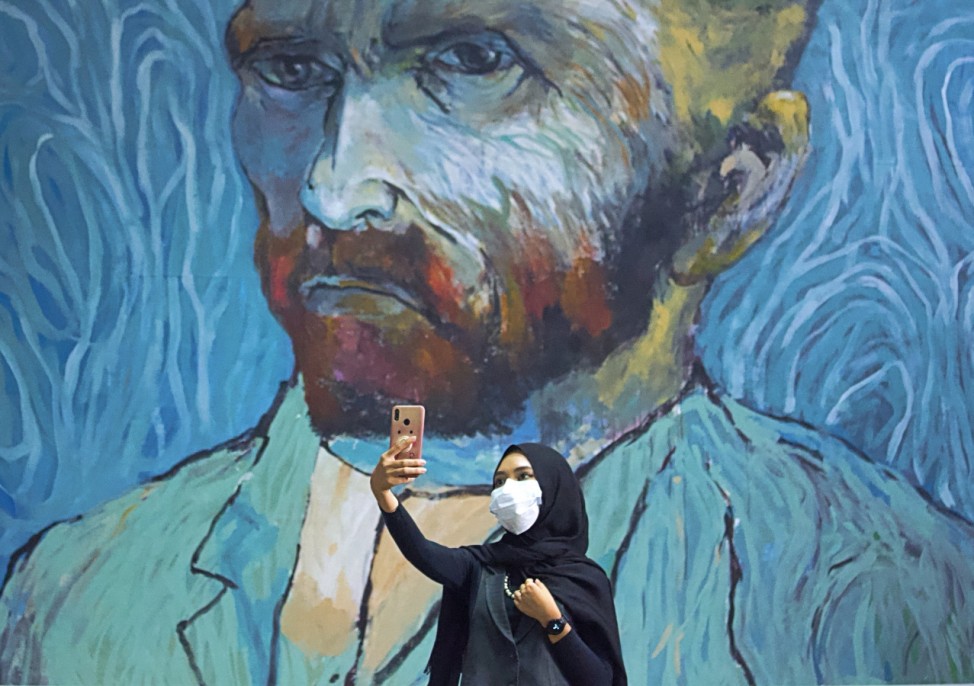 A visitor wearing a protective face mask takes a selfie near an art-wall painted by Indonesian artist Hanafi at Kertas Gallery during an exhibition in Depok